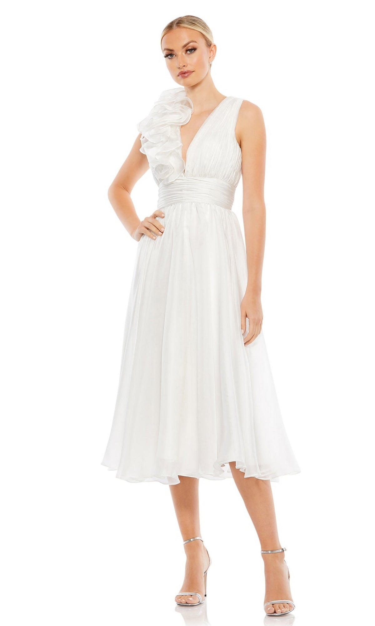 A woman models the Short Wedding Guest Dress 70165 by Mac Duggal, a sleeveless white A-line dress with a ruched ruffled bodice, deep V-neck, and one-shoulder detail, paired with silver high-heeled sandals.